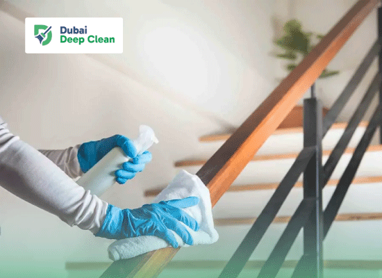 Professional deep cleaning service in Dubai showing a cleaner sanitizing a wooden staircase railing with gloves and spray.