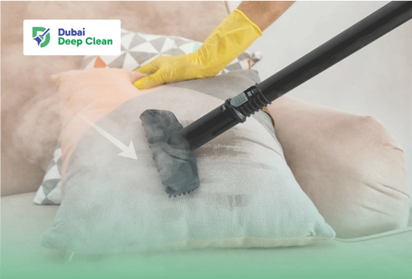 A professional cleaner in yellow safety gloves using a specialized steam cleaner head to sanitize a soft pillow on a bed, releasing visible steam to kill bacteria and dust mites.